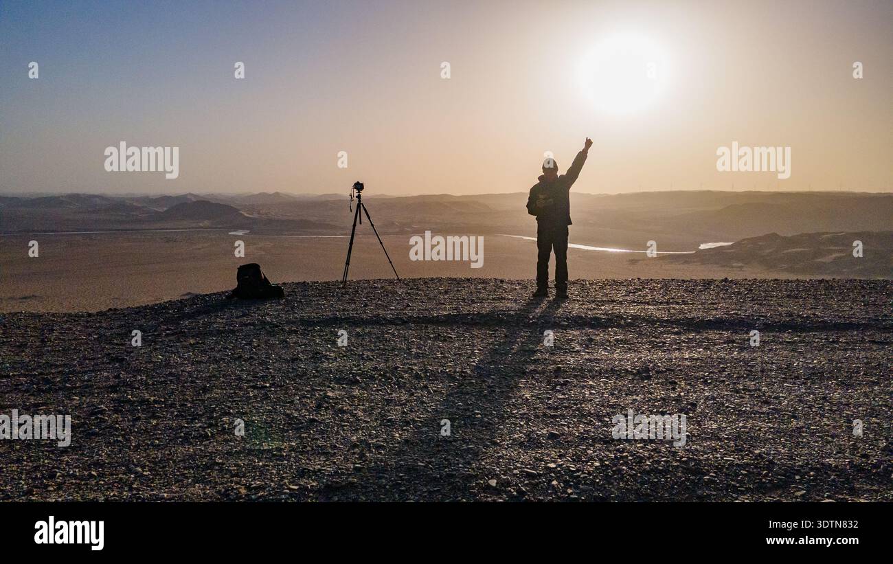 Silhouette d'un photographe utilisant un appareil photo monté sur trépied dans un paysage désertique au lever du soleil. Banque D'Images