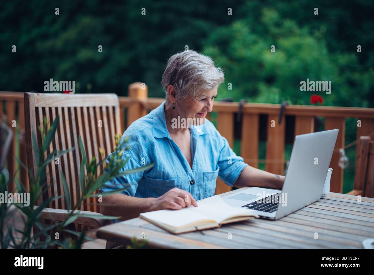 Femme mature assise sur le balcon avec ordinateur portable, travaillant à distance. Banque D'Images