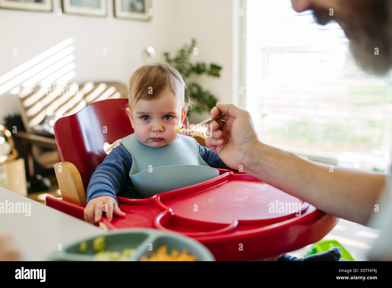 Père attentionné qui nourrit les tout-petits pendant les repas à la maison. Banque D'Images