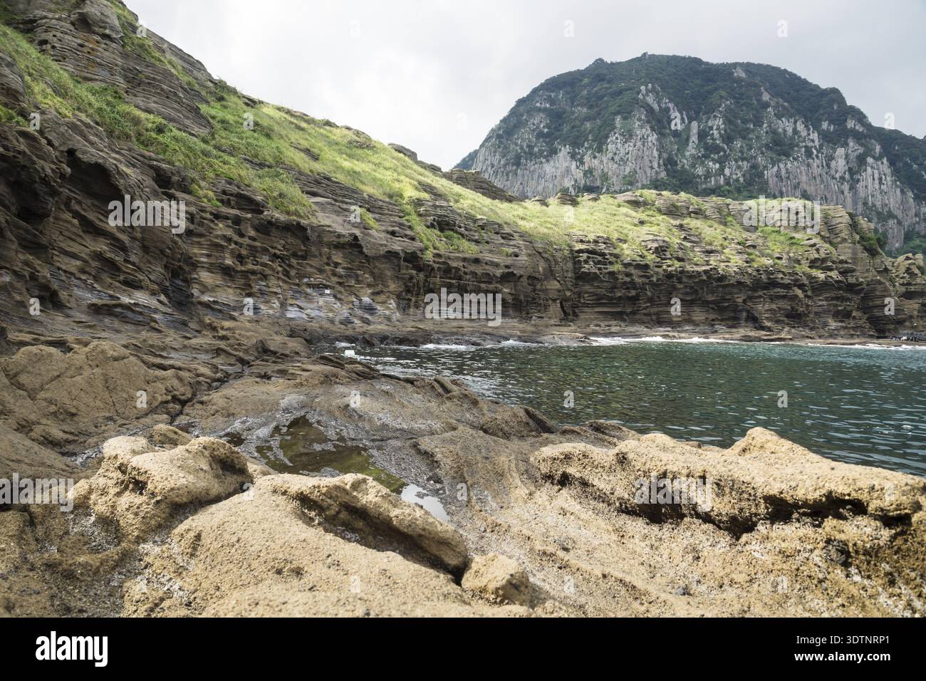 La formation de lave de falaises avec partie supérieure verte avec vue sur le mont Sanbangsan à Yongmeori Beach, Sanbang-ro, l'île de Jeju, Corée du Sud Banque D'Images