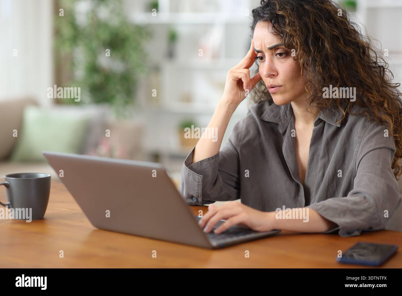 Femme adulte inquiète à la maison vérifiant les mauvaises nouvelles sur ordinateur portable sur une table en bois Banque D'Images