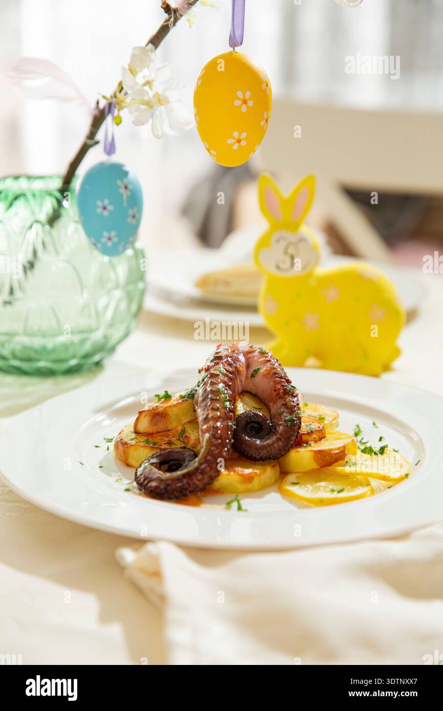Poulpe grillé gourmand avec pommes de terre servi sur une élégante table de Pâques. Plat de fruits de mer printanier festif avec décorations de vacances Banque D'Images