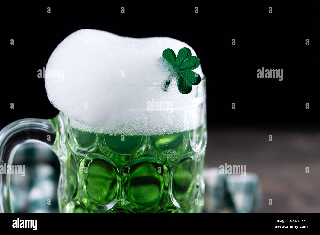 Mug de bière vert versant avec mousse pour la fête de Patrick sur table en bois noir et fond noir Banque D'Images