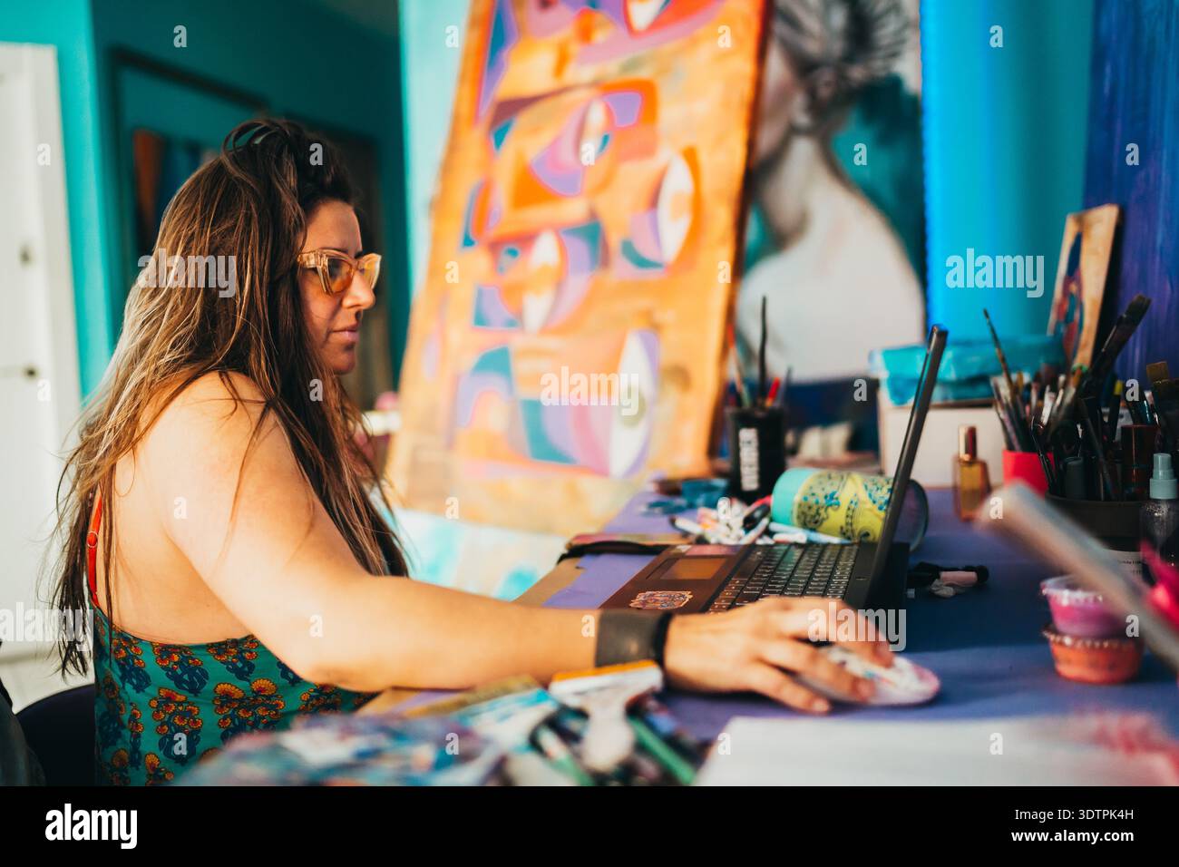 Femme artiste travaillant sur ordinateur portable avec des peintures dans studiobehind Banque D'Images