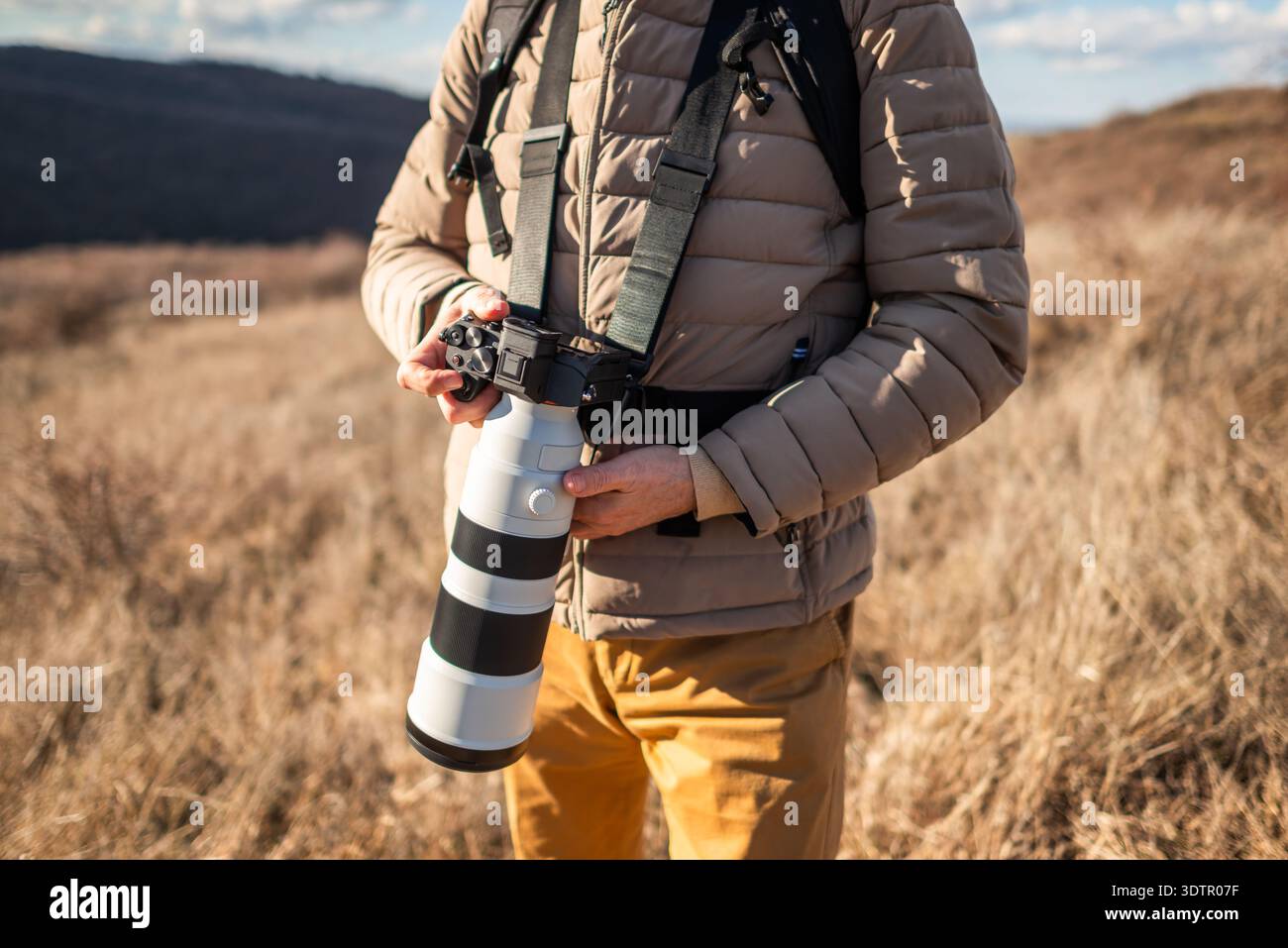 Gros plan d'un photographe en plein air au milieu des prairies sèches, à l'aide d'un objectif zoom long pour photographier la nature par temps clair. Banque D'Images