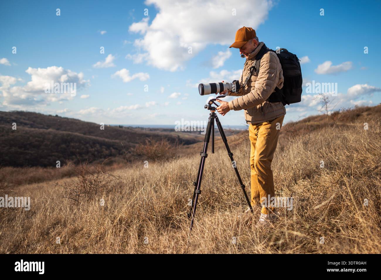 Photographe expérimenté de la faune utilisant un trépied et fixant un grand téléobjectif sur un paysage de campagne ouvert par jour ensoleillé. Banque D'Images