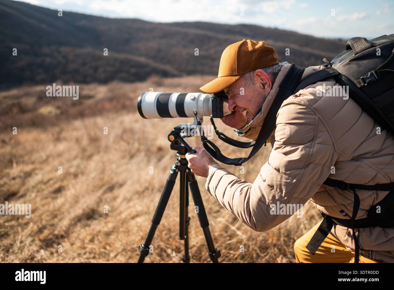 Une vue rapprochée d'un photographe animalier utilisant un trépied et visant un grand téléobjectif à travers un paysage de campagne ouvert par jour ensoleillé. Banque D'Images