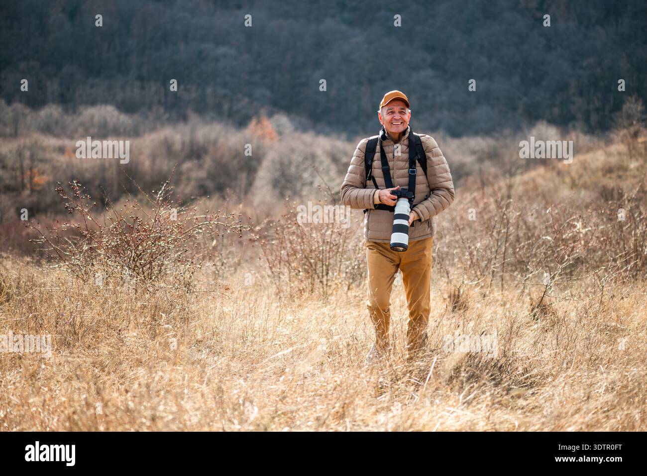 Un photographe animalier ou paysagiste se concentre sur son appareil photo alors qu'il est entouré d'un terrain d'herbe sèche sur la montagne. Banque D'Images