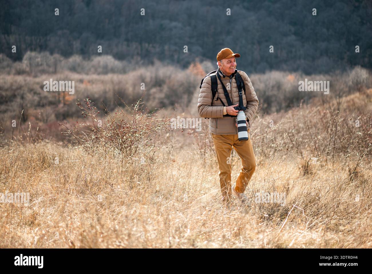 Un photographe animalier ou paysagiste se concentre sur son appareil photo alors qu'il est entouré d'un terrain d'herbe sèche sur la montagne. Banque D'Images