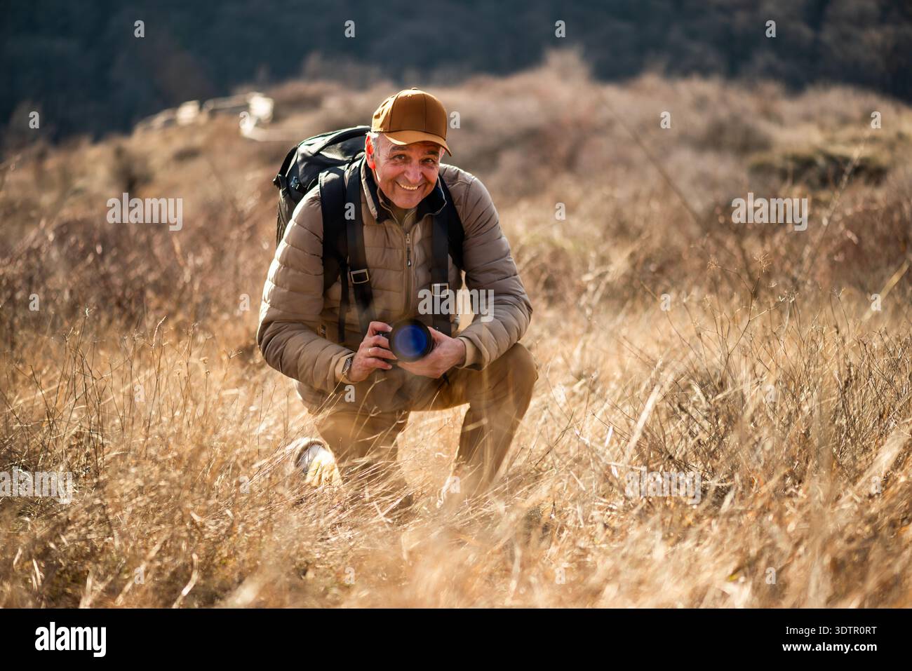 Un photographe de la nature s'agenouille dans un champ d'herbe sèche, ajustant soigneusement les paramètres de son appareil photo tout en capturant des détails rapprochés du paysage en guerre Banque D'Images