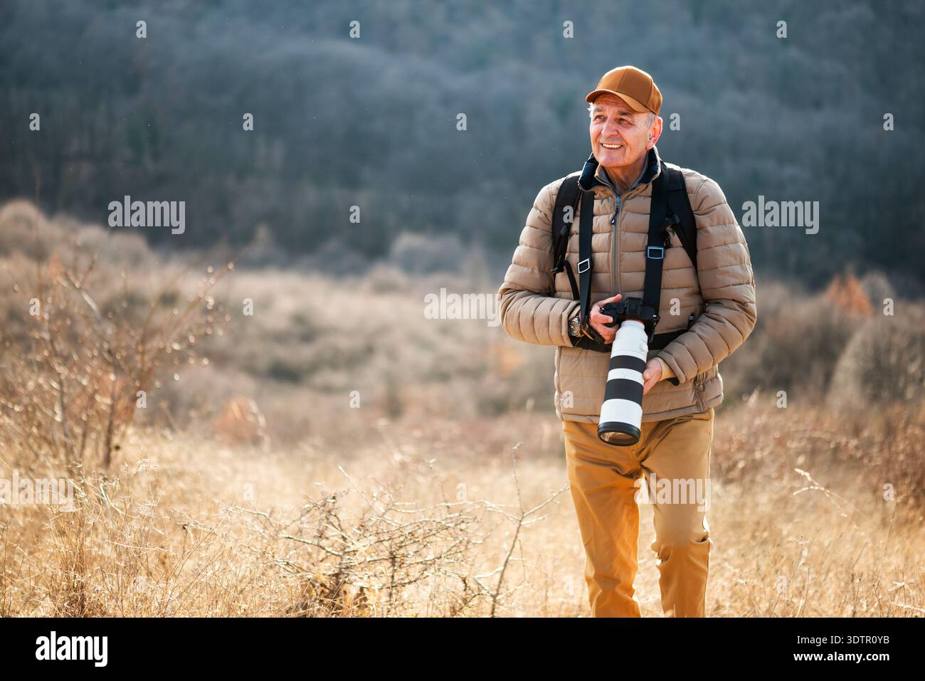 Un photographe animalier ou paysagiste se concentre sur son appareil photo alors qu'il est entouré d'un terrain d'herbe sèche sur la montagne. Banque D'Images