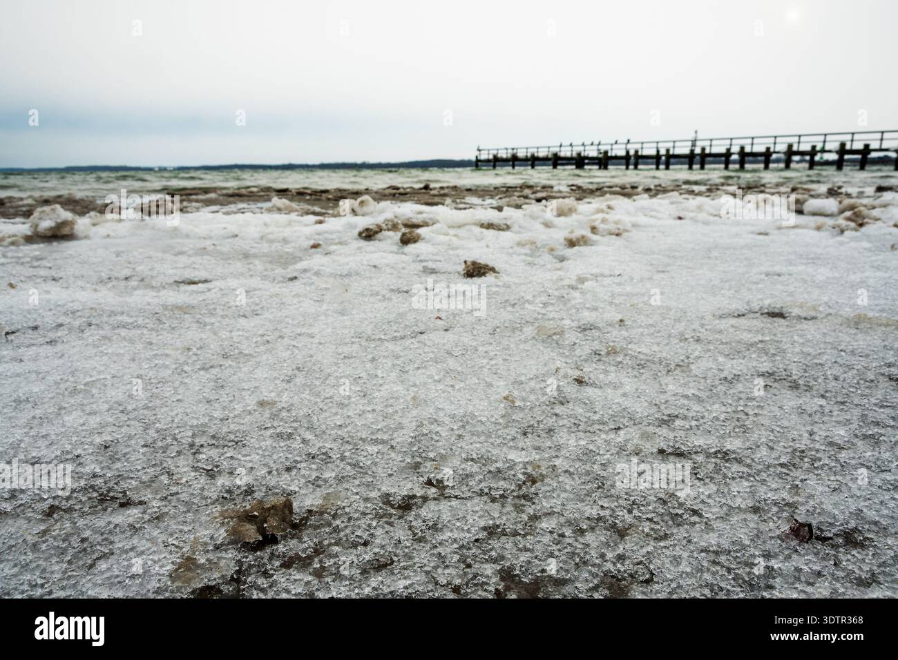 Rivage gelé avec texture de glace rugueuse le long de la mer Baltique et jetée lointaine sous le ciel froid de l'hiver. Banque D'Images