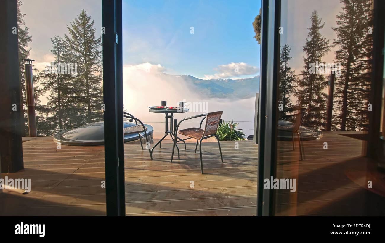 Petit déjeuner balcon cabine de montagne au-dessus des nuages. Terrasse en bois confortable avec table et chaises surplombe la vallée brumeuse et les montagnes lointaines, créant un Banque D'Images