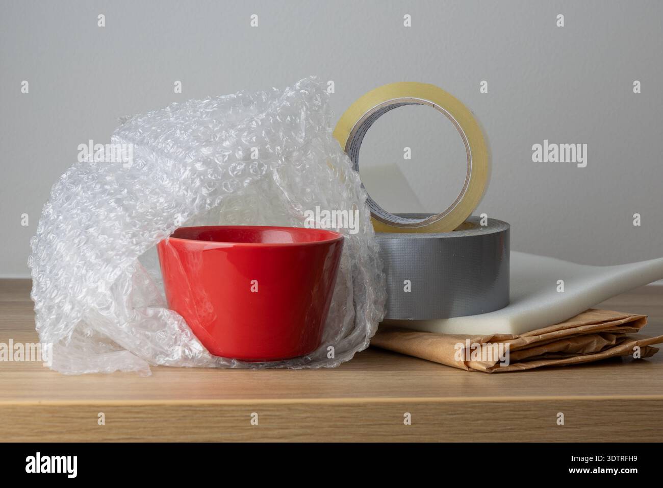 Un bol rouge enveloppé dans du papier bulle et du ruban adhésif, prêt pour l'expédition ou le stockage en toute sécurité. Banque D'Images
