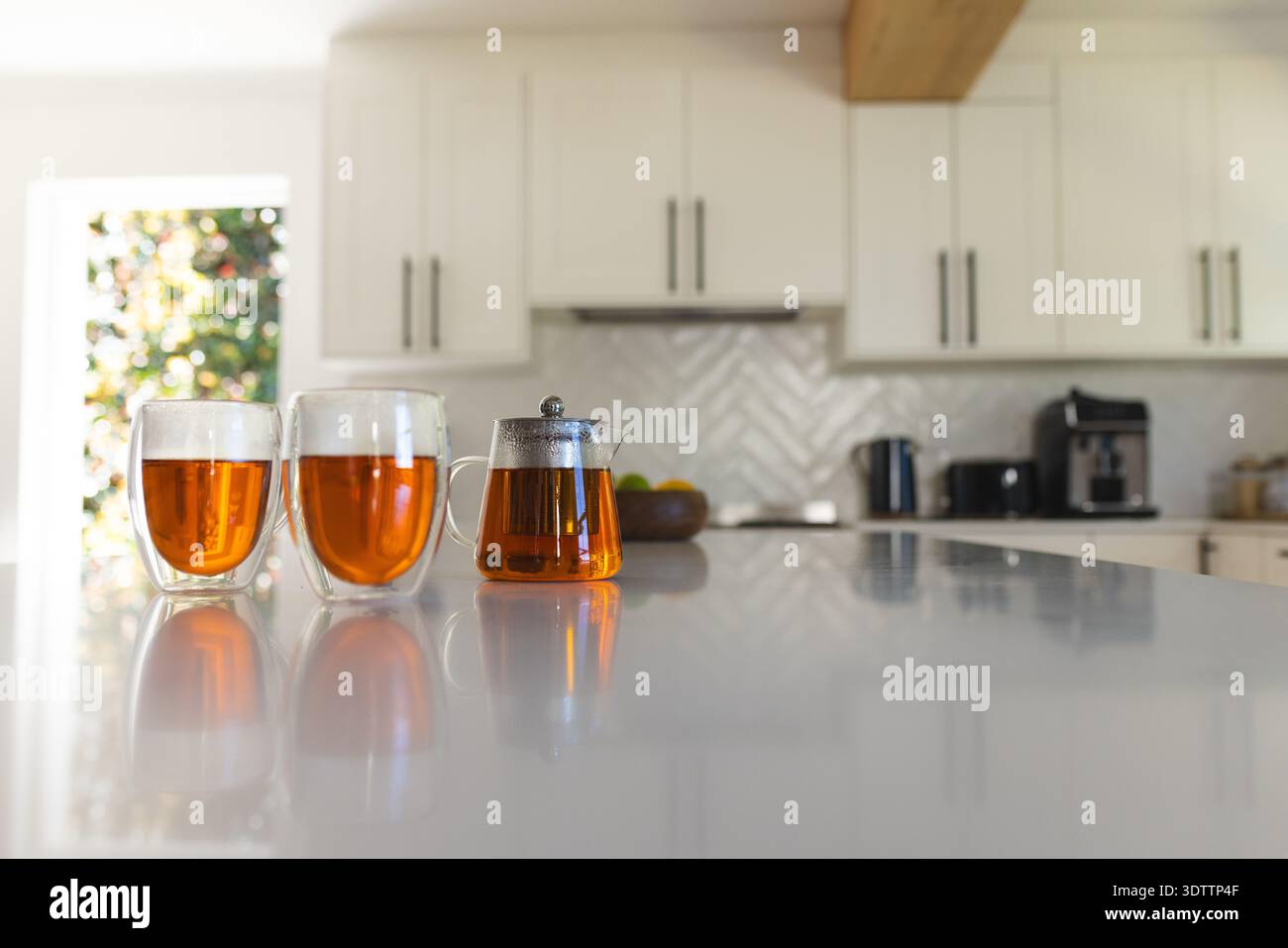Deux tasses en verre à double paroi et une théière en verre reflètent le thé ambré sur une île blanche brillante Banque D'Images