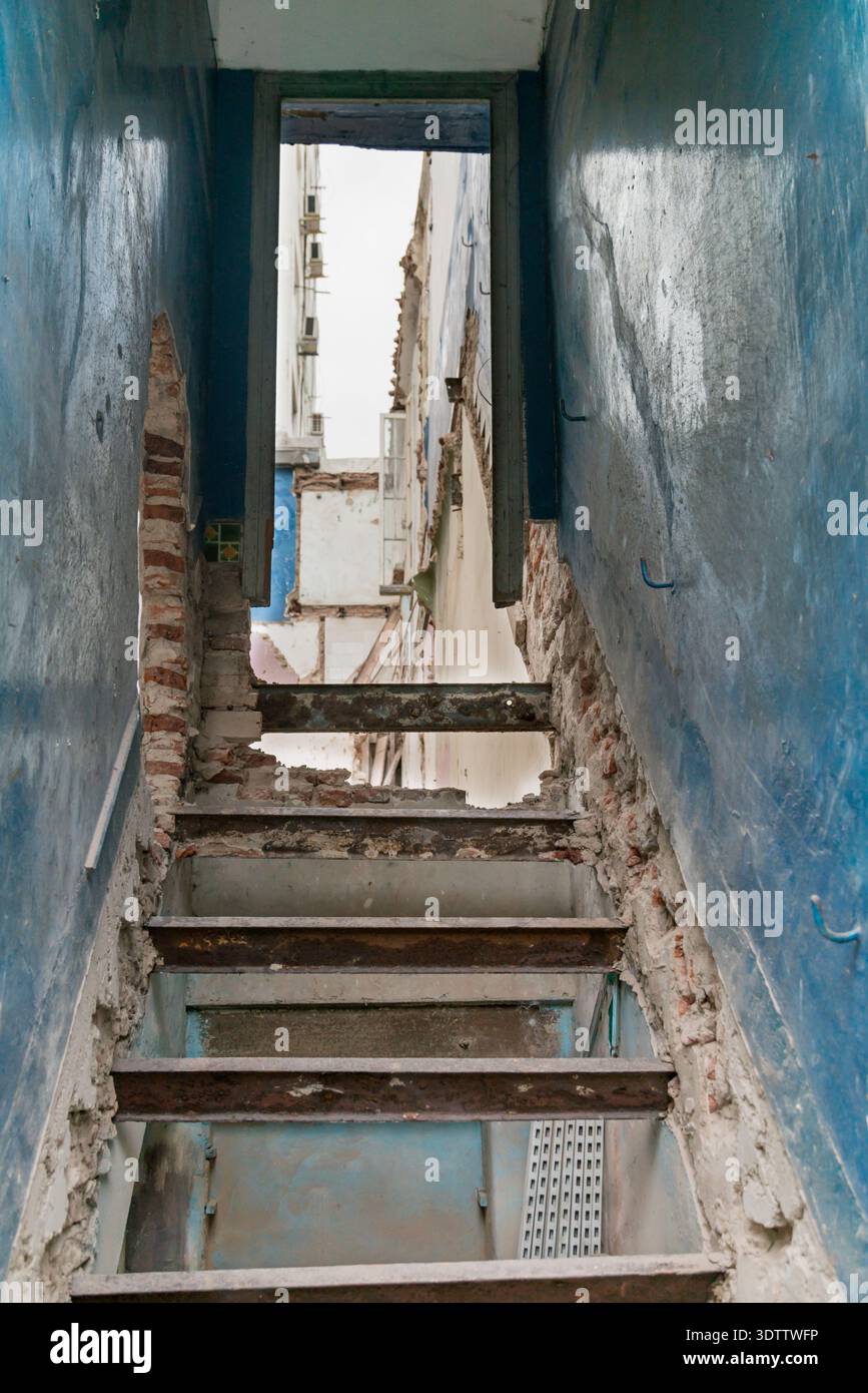 Un escalier abrupt et gravement détérioré, avec des briques apparentes, descend entre deux murs bleus qui sont en cours de démolition. Banque D'Images