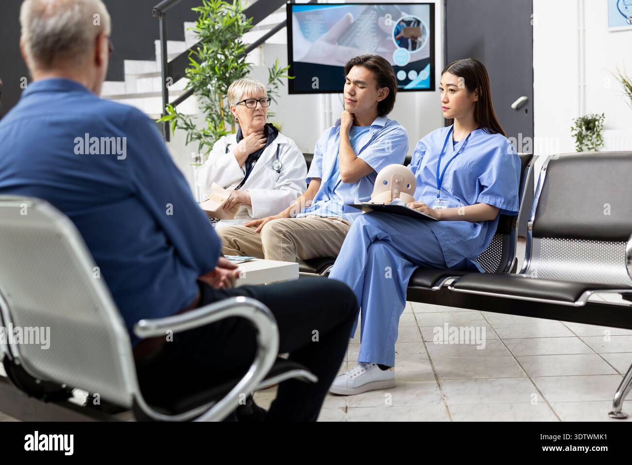 Le jeune homme adulte explique les symptômes aux médecins, exprimant la tension musculaire et l'inconfort lors de la consultation hospitalière de routine. Le patient masculin est assis dans la salle d'attente de la clinique avec le personnel médical féminin. Banque D'Images