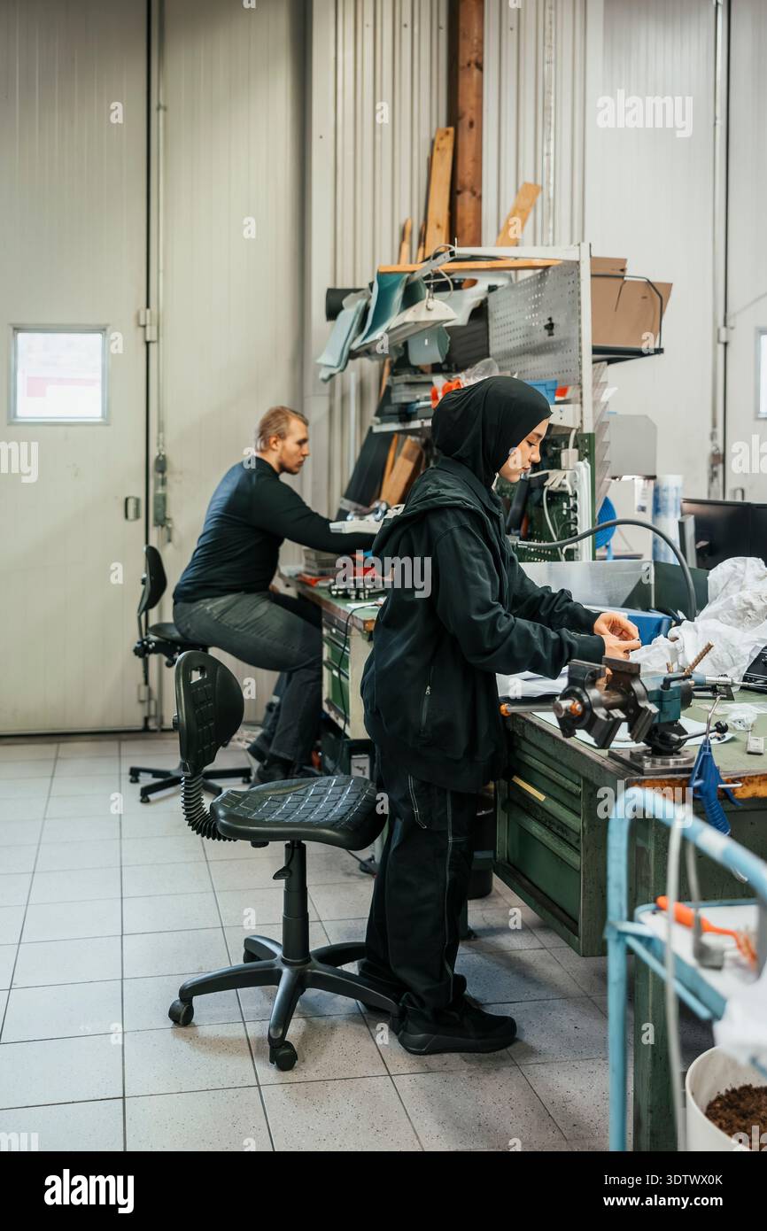 Pleine longueur de travailleuse d'usine assemblant des pièces en usine Banque D'Images