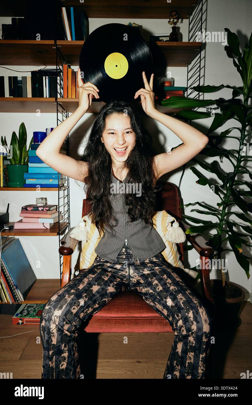 Portrait de femme heureuse avec tenir un disque vinyle tout en étant assis sur une chaise à la maison Banque D'Images