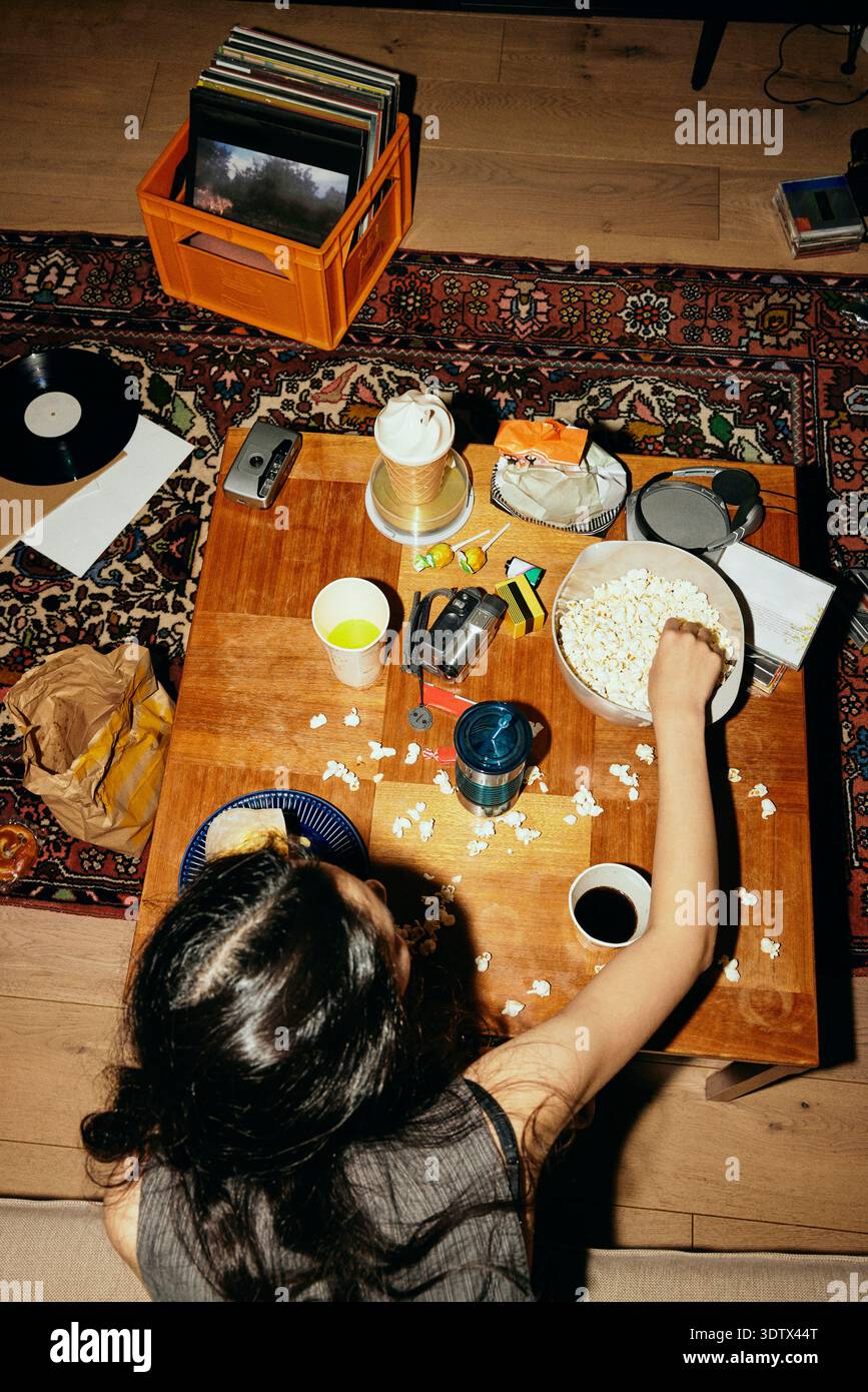 Vue en angle élevé d'une femme mangeant du pop-corn assise à une table désordonnée Banque D'Images