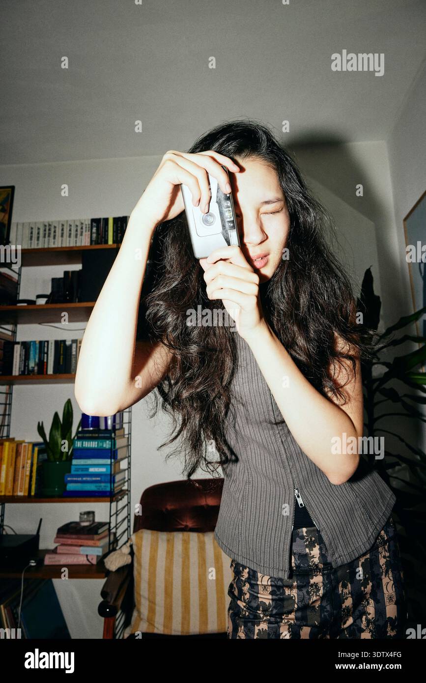 Jeune femme cliquant sur des photos avec caméra de film à la maison Banque D'Images