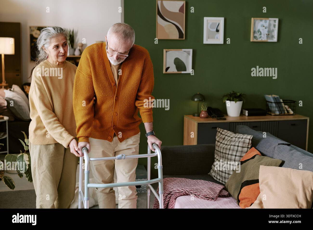 Femme caucasienne senior aidant homme caucasien senior utilisant Walker à l'intérieur Banque D'Images
