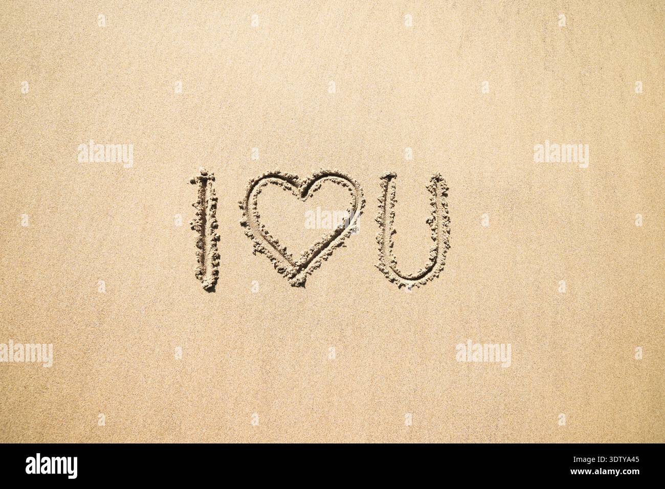 Je t'aime. Texte avec un coeur écrit dans le sable doré. Banque D'Images