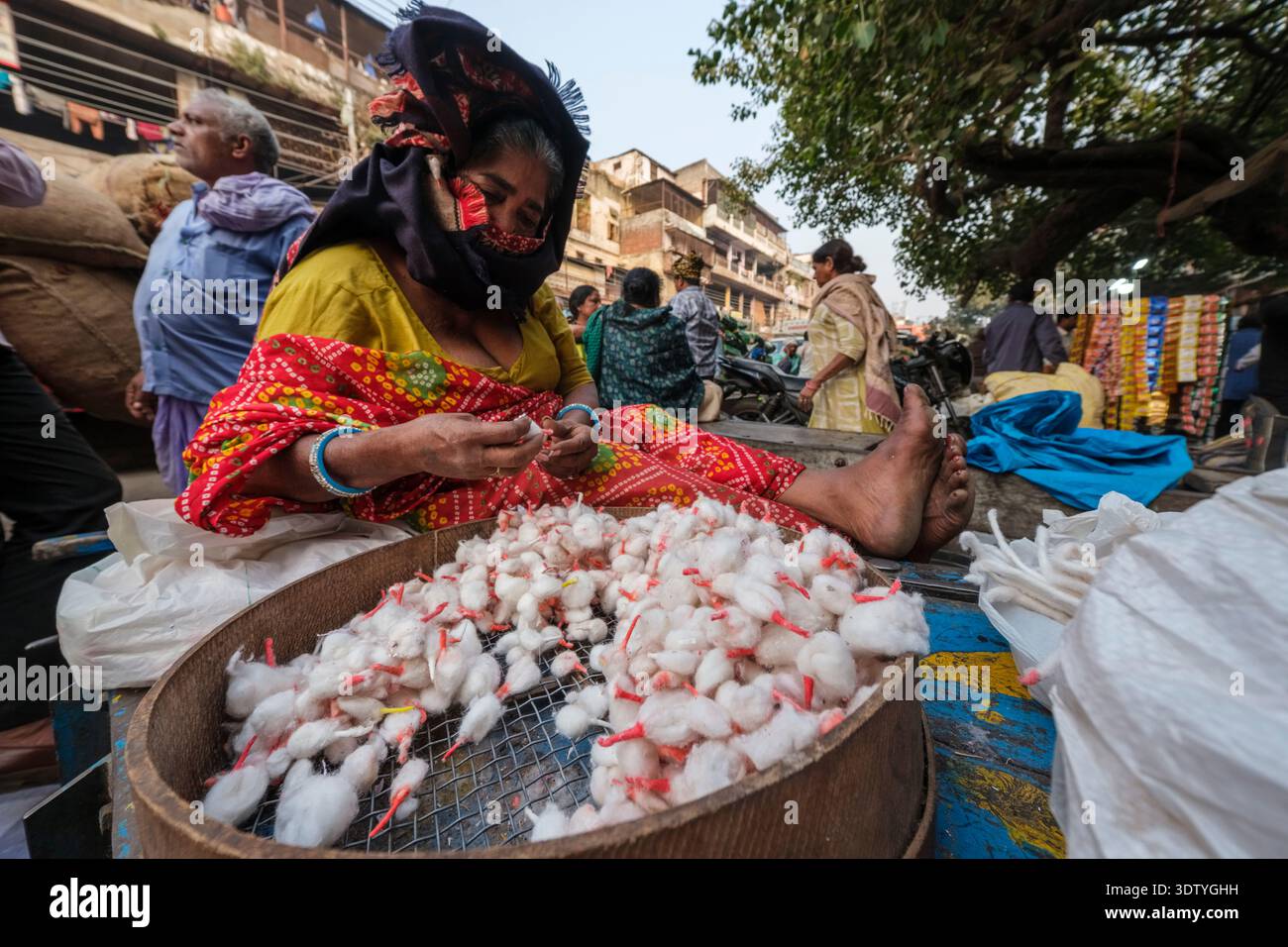 Vendeur de rue assis sur Chandni Chowk dans le vieux Delhi, préparant des mèches de coton dans un tamis. Les passants et les bâtiments sont visibles au loin. Banque D'Images