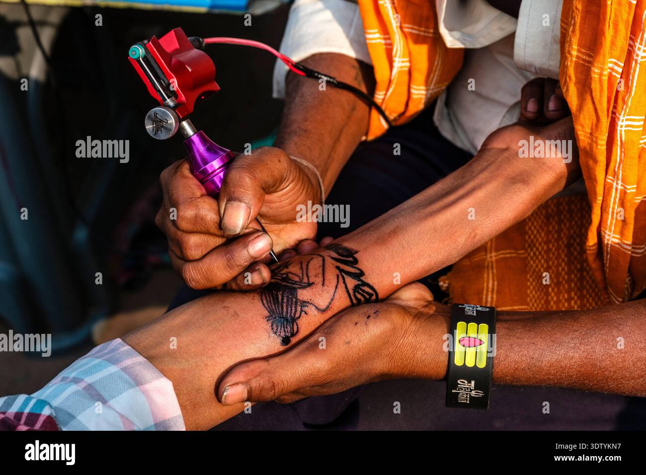 Un artiste utilise une machine à tatouer pour encrer un dessin détaillé sur l'avant-bras d'une personne à New Delhi. Banque D'Images