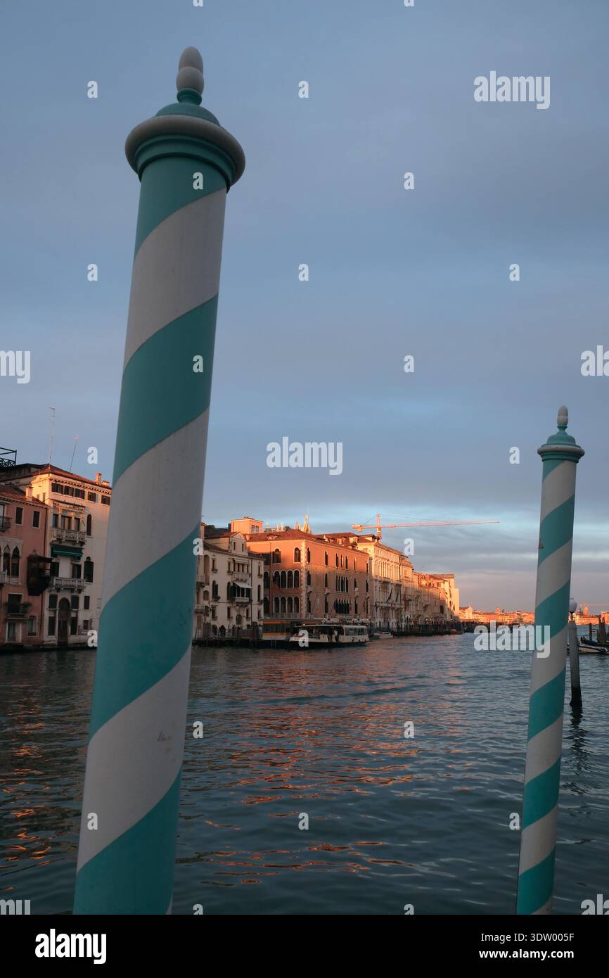 Poteaux rayés bleus et blancs le long du Grand canal dans la lumière du soleil de fin d'après-midi, Venise Italie Banque D'Images