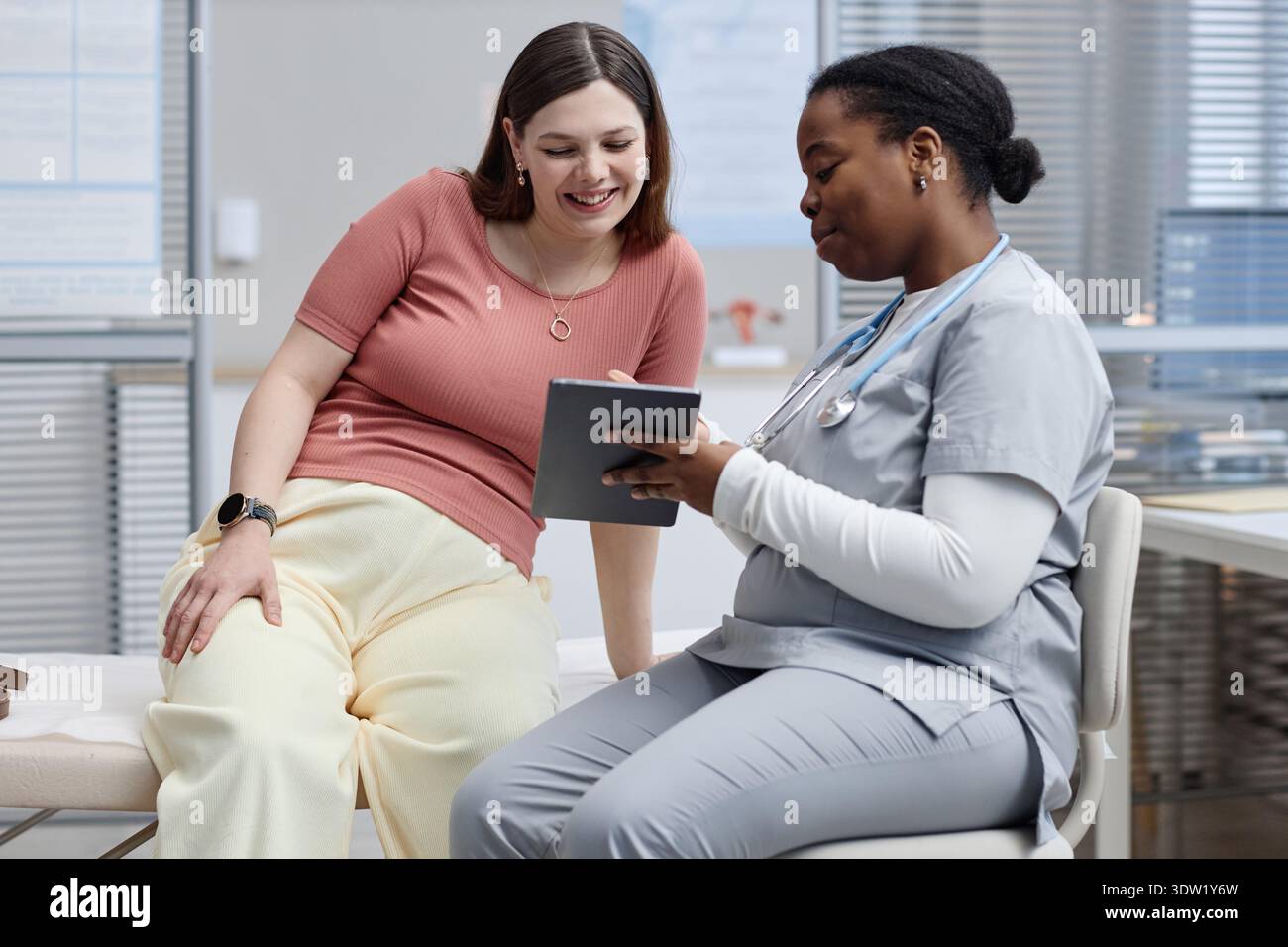 Femme caucasienne d'âge moyen souriant tandis que Black Female Nurse évaluant Tablet Banque D'Images