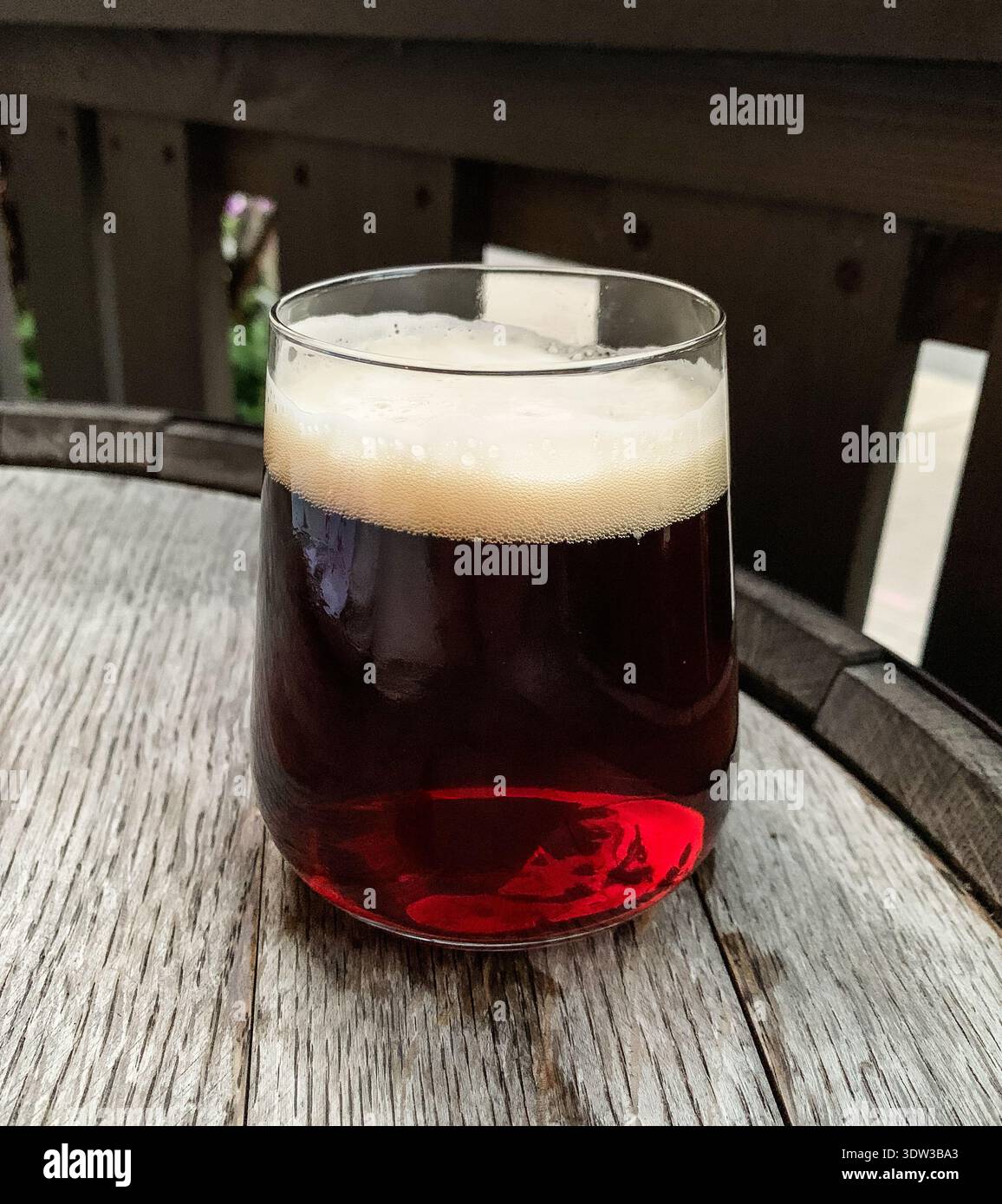 Gros plan d'un verre de bière brune avec une tête en mousse crémeuse sur une table rustique en tonneau en bois. Image de concept de brasserie et de pub. Banque D'Images