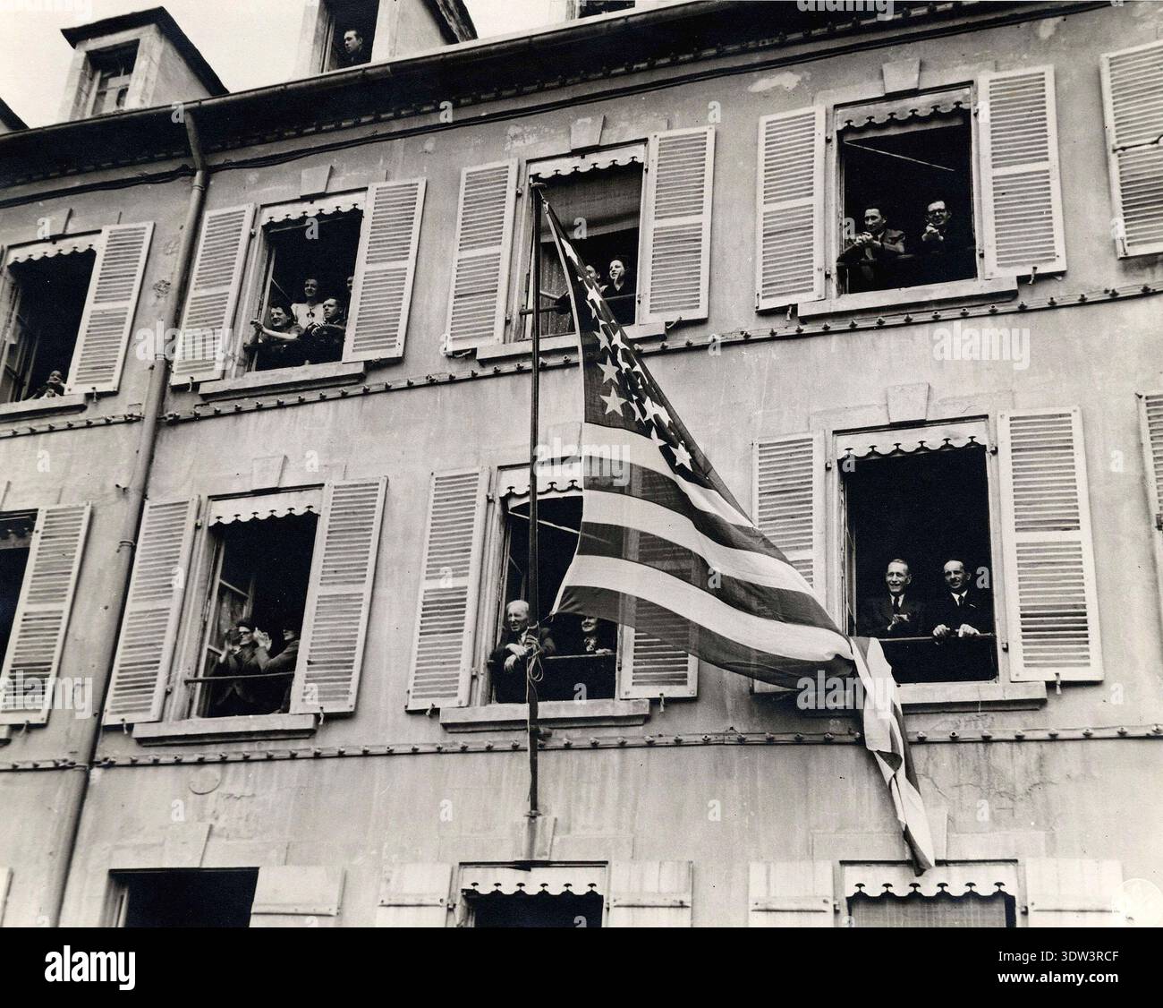 Les gens se sont rassemblés aux fenêtres d'un immeuble résidentiel de Cherbourg récemment libéré qui porte le drapeau américain. Les gens regardent les débats dans la rue. Banque D'Images