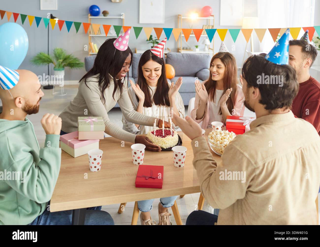 Groupe de jeunes heureux portant des chapeaux de fête applaudissant et félicitant la femme d'anniversaire avec un gâteau. Banque D'Images