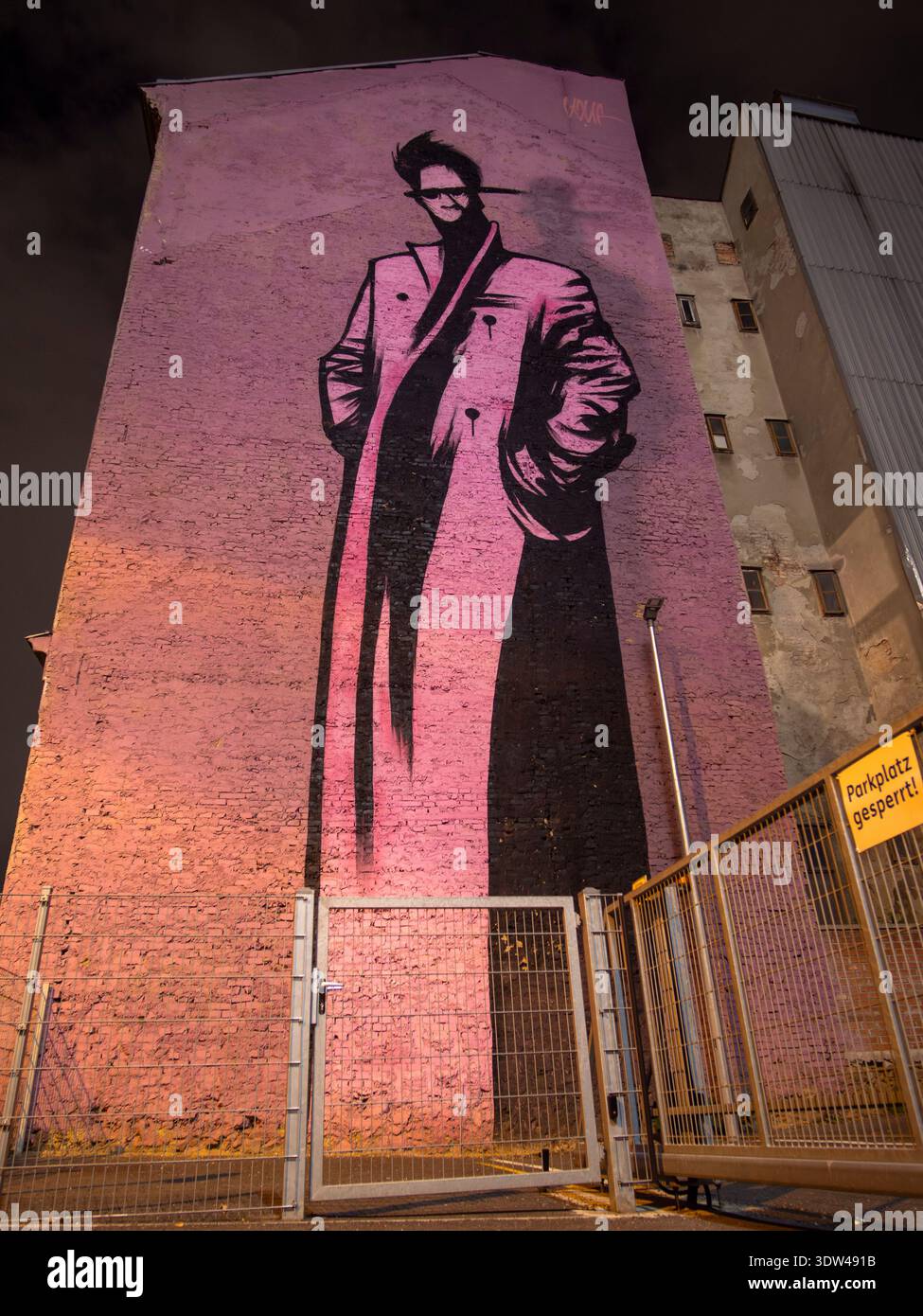 Grande murale de nuit d'homme en long manteau sur le mur du bâtiment de Vienne, style rose et noir, art urbain dramatique la nuit. Banque D'Images