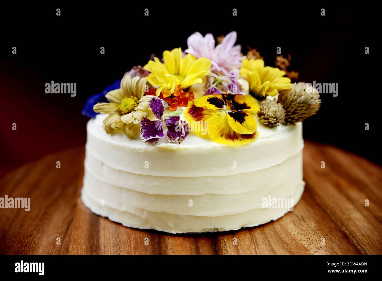 Élégant gâteau blanc crème décoré de fleurs comestibles colorées vibrantes Banque D'Images
