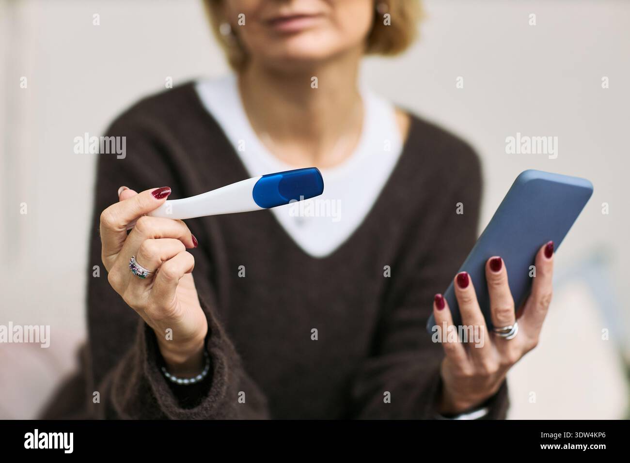 Femme caucasienne d'âge moyen tenant le test d'ovulation dans une main et smartphone dans l'autre, démontrant la technologie de surveillance de la santé de la femme pour la gestion de la santé reproductive Banque D'Images