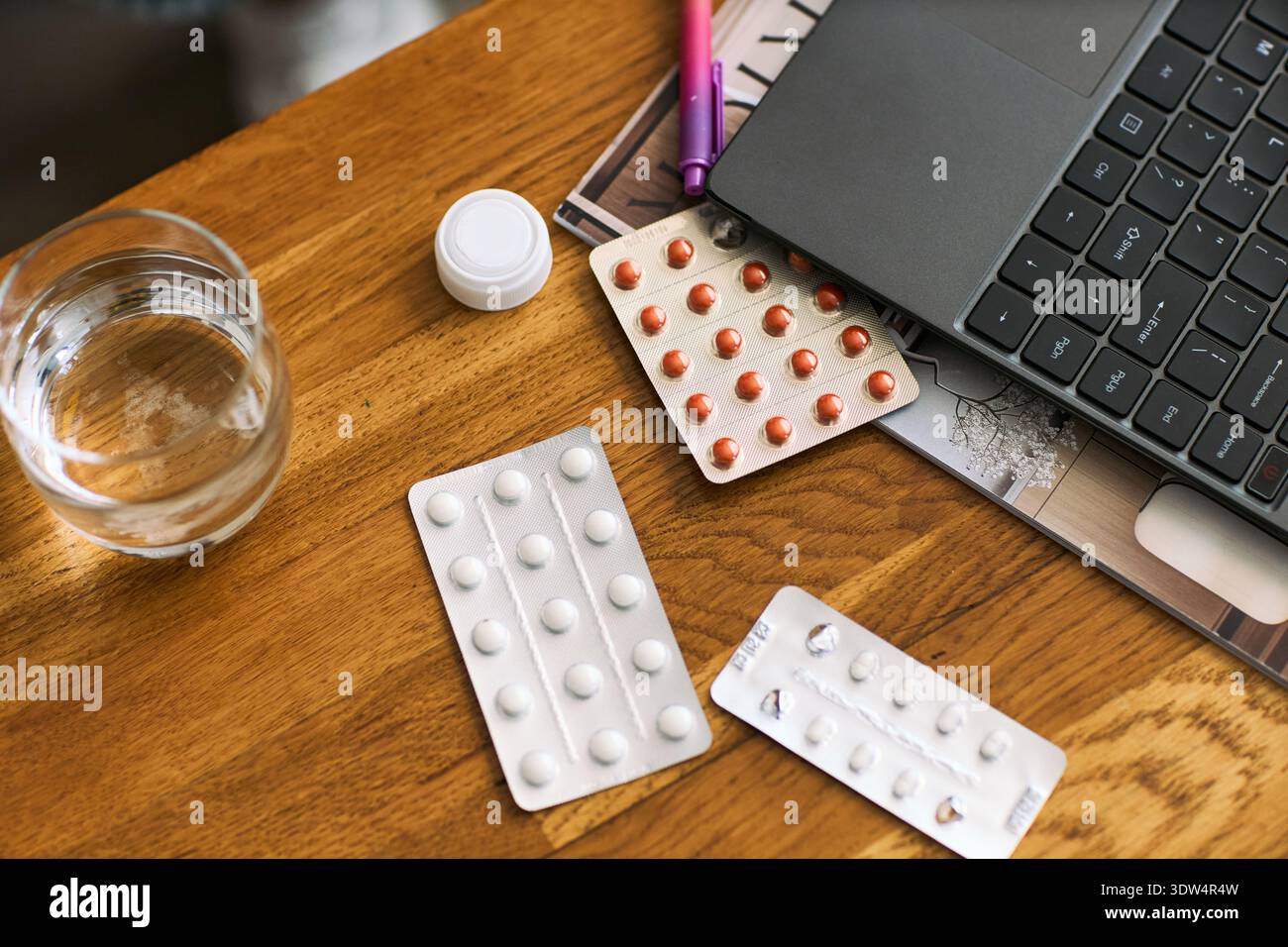 Gros plan montrant des blisters de pilules, un verre d'eau, un ordinateur portable ouvert sur une table en bois, illustrant le concept de santé femtech avec un accent sur les médicaments et la gestion numérique de la santé Banque D'Images