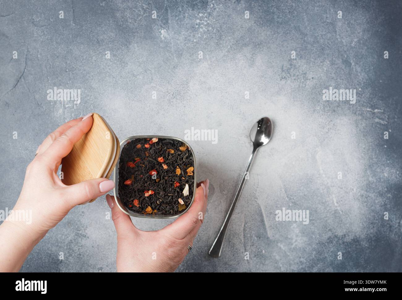 Thé noir aux feuilles avec des additifs de fruits (fraise, framboise, pomme, poire, feijoa) dans un pot en verre dans les mains des femmes sur un fond gris. Un délicieux et Banque D'Images