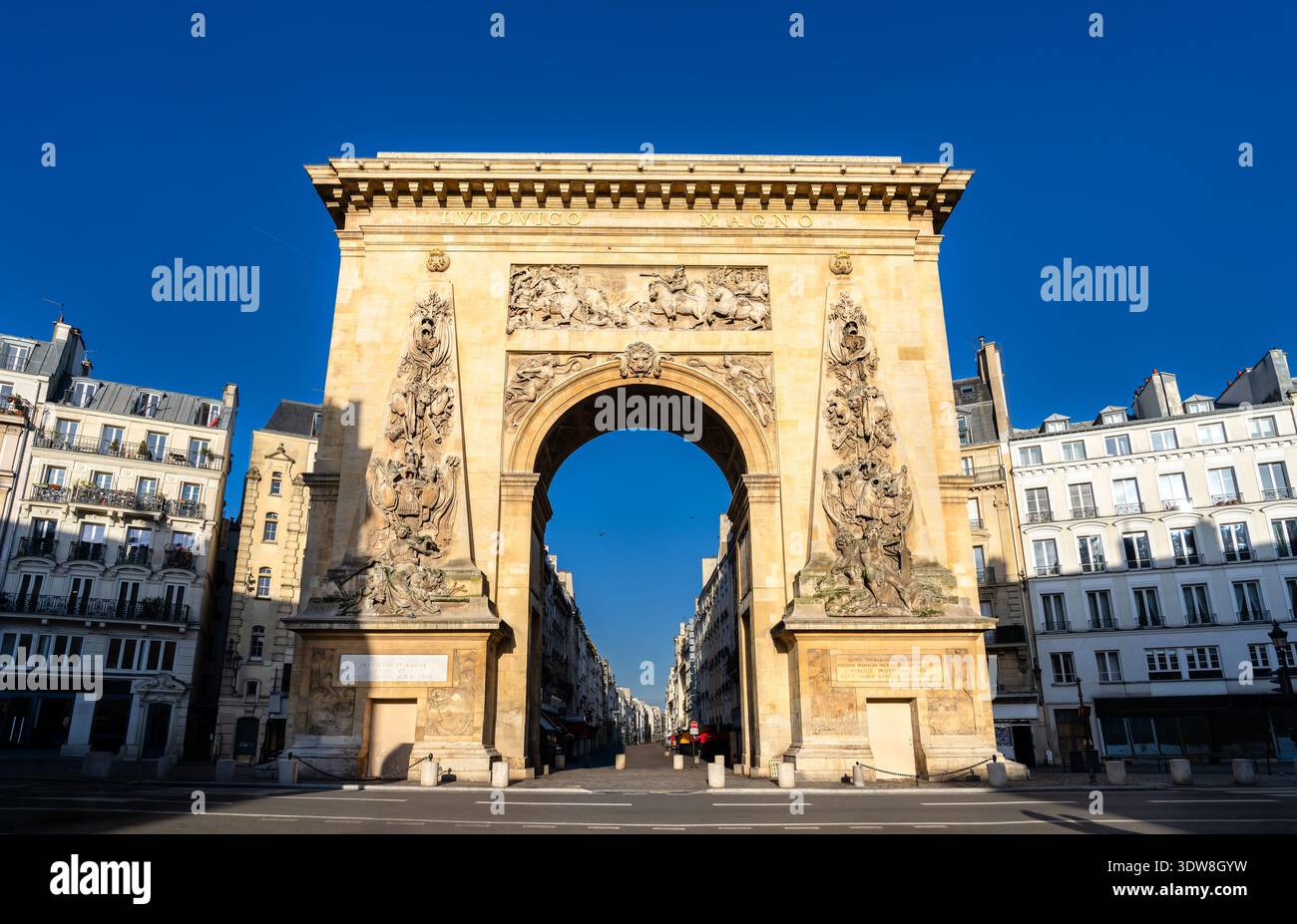 Vue panoramique ensoleillée sur l'arc de triomphe historique de la porte Saint-Denis avec des sculptures en bas-relief complexes et des bâtiments parisiens classiques à Paris, France. Banque D'Images