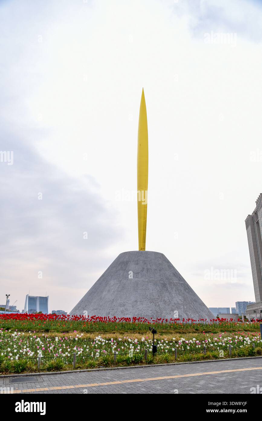 L'emblématique sculpture en forme de flèche à flamme dorée s'élève d'une base pyramidale en béton entourée de tulipes rouges et blanches à Odaiba, Tokyo. Banque D'Images