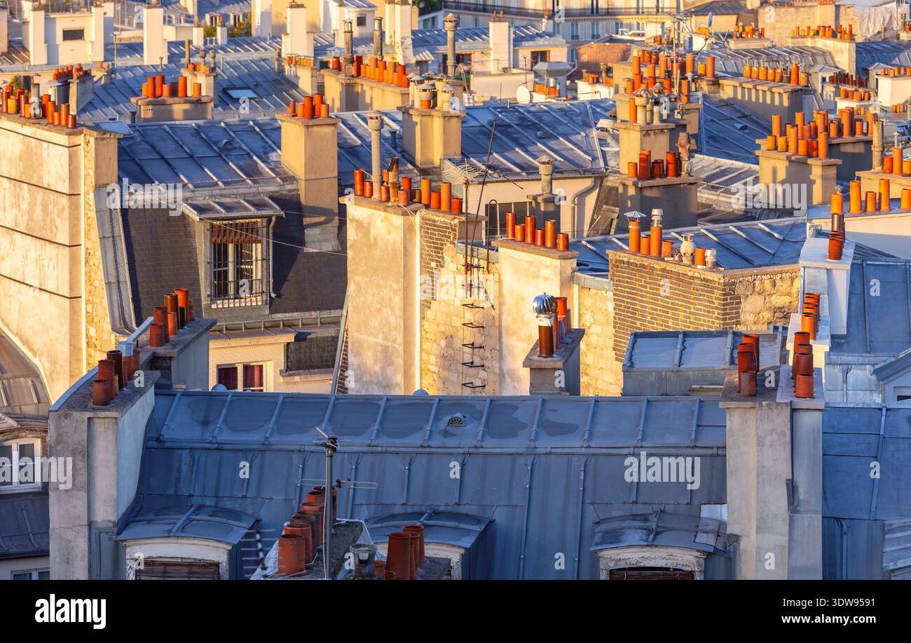 Cheminées traditionnelles en argile avec capuchons métalliques sur un toit de la ville illuminées par la lumière chaude du lever du soleil. Détail architectural urbain Banque D'Images