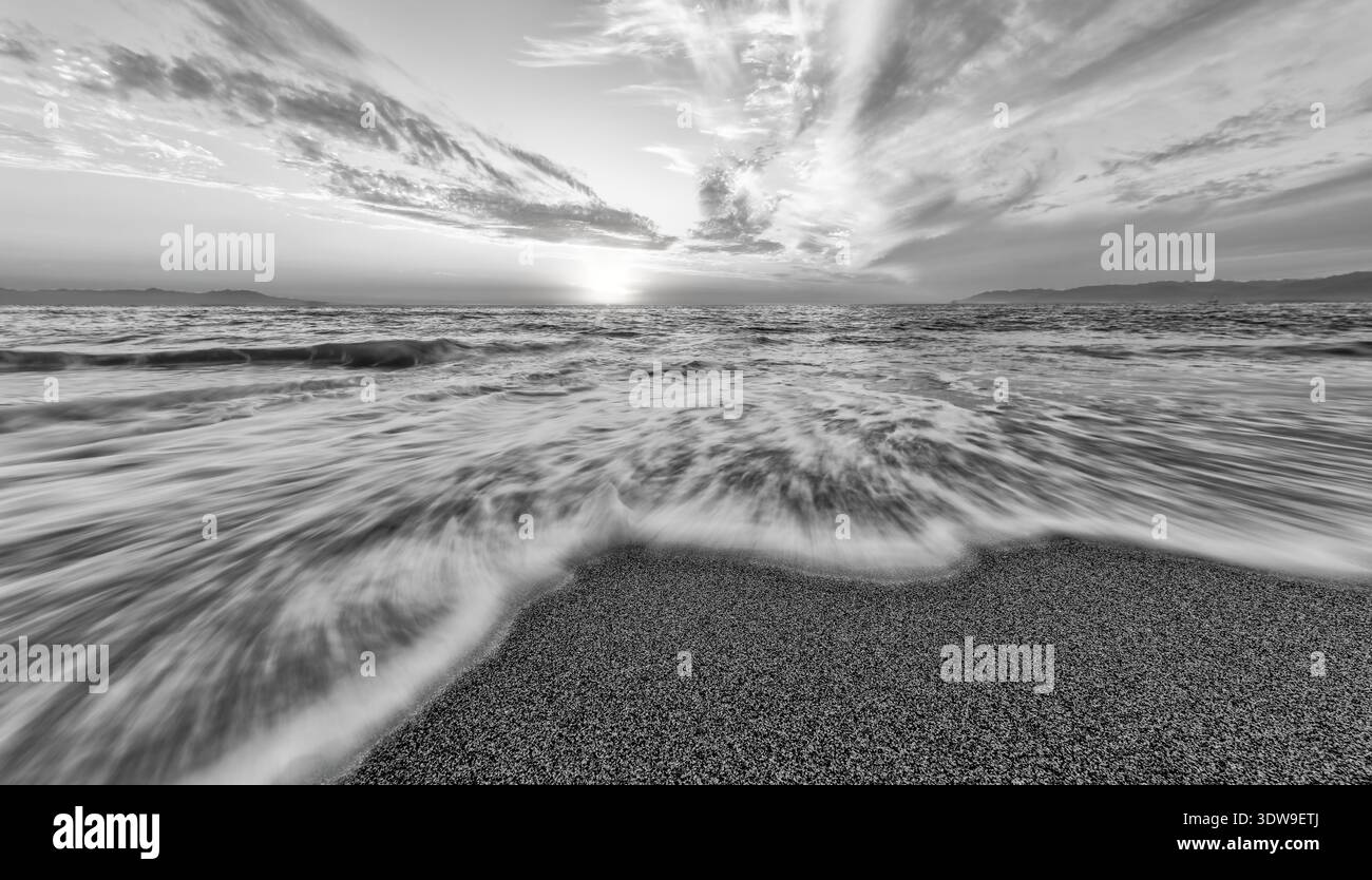 Un coucher de soleil noir et blanc Ocean Seascape avec Une vague se brisant sur le rivage noir et blanc Banque D'Images