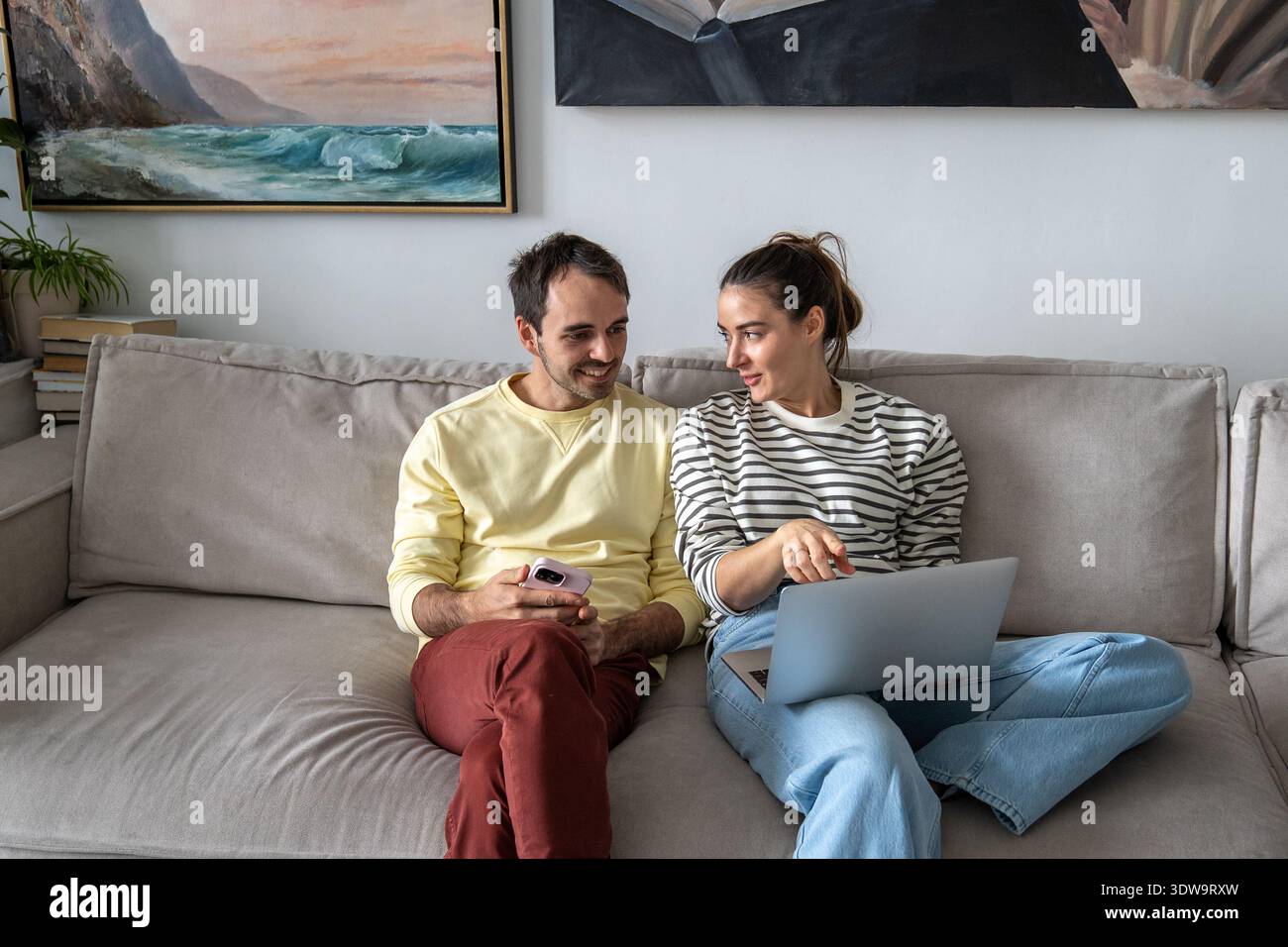 Heureux couple marié profitant du temps à la maison le week-end, se relaxant sur le canapé regardant le film drôle en ligne. Banque D'Images