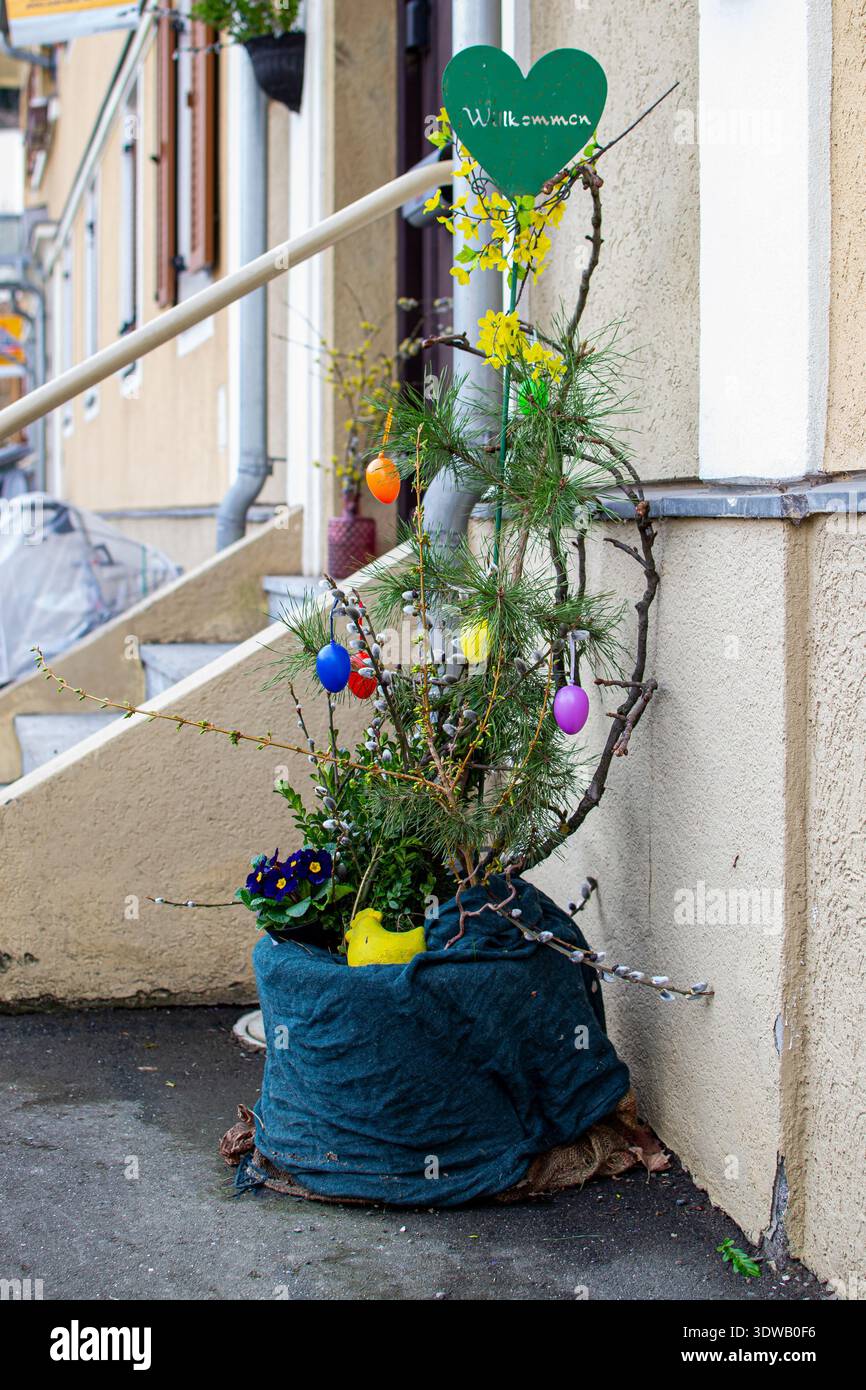Décoration festive de Pâques avec plantes printanières en pot, œufs peints et signe de coeur de bienvenue à l'entrée de la maison. Concept de décoration extérieure saisonnière. Banque D'Images