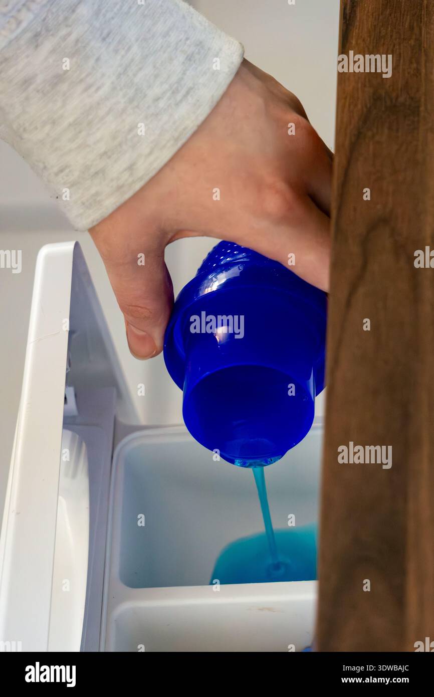 Vue rapprochée de la lessive liquide bleue versée dans le compartiment à lessive d'une machine à laver. Banque D'Images