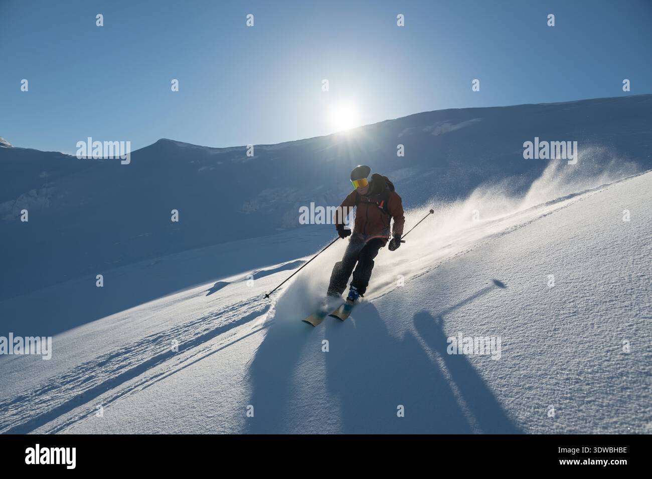 Un skieur sculpte à travers la poudre fraîche sur une pente ensoleillée, entourée par le ciel bleu et les montagnes. Le groupe aime l'aventure hors-piste avec une expérience en hélicoptère, capturant la liberté et les sensations fortes en hiver en plein air. || autorisation du modèle Banque D'Images