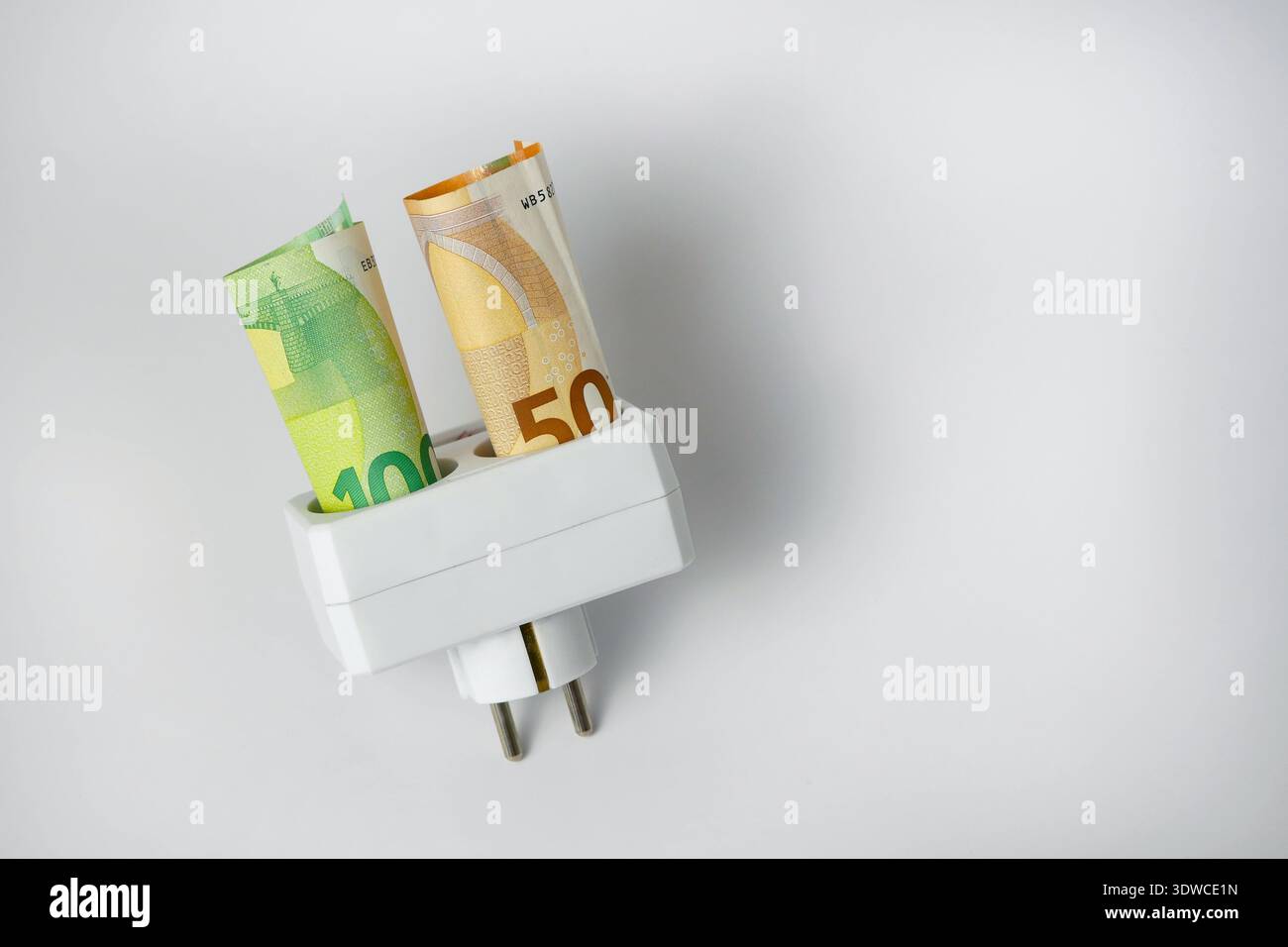Billets en euros dans la prise de prise électrique sur fond blanc. Concept des coûts de l'énergie, la hausse des prix de l'électricité, l'inflation, les factures de services publics et financiers Banque D'Images