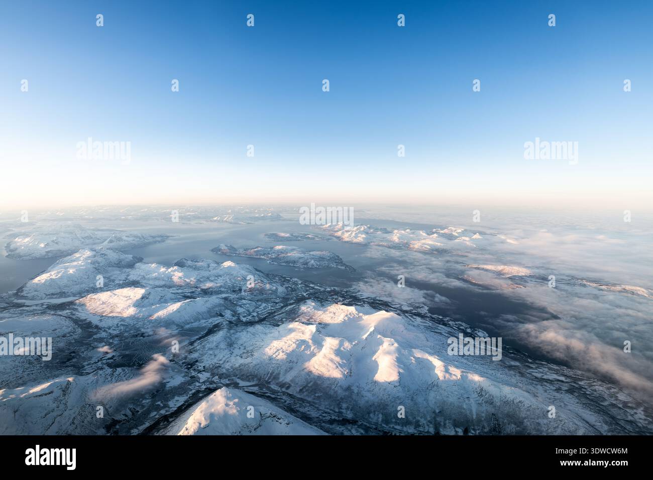 Vue aérienne mettant en évidence un vaste paysage hivernal immaculé avec des sommets ensoleillés et des fjords sereins Banque D'Images