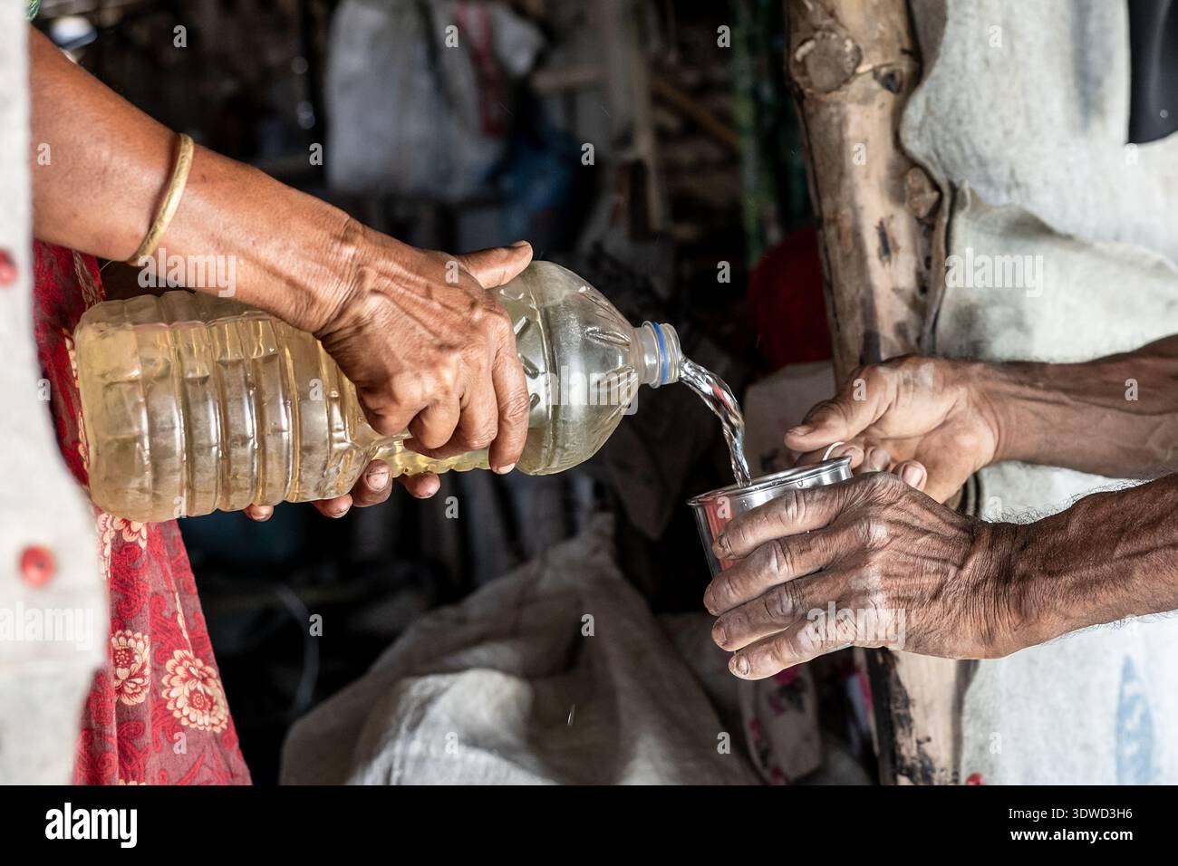 Satkhira, Bangladesh - 21 octobre 2025 : vue de mains altérées versant de l'eau d'une bouteille en plastique dans une petite tasse en métal, un moment poignant de suste Banque D'Images